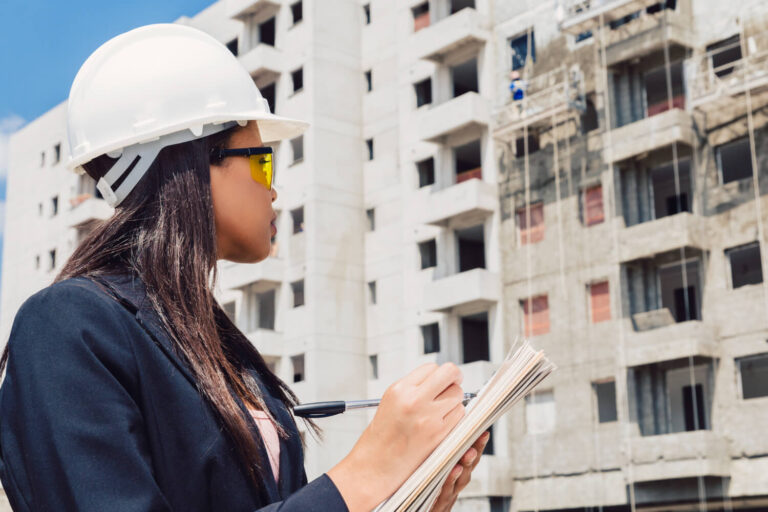 african-american-lady-safety-helmet-writing-notepad-near-building-construction (1)